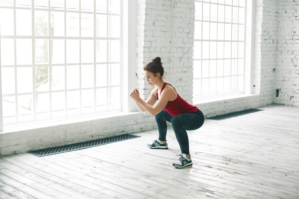 A woman does body-weight squats in a gym. 