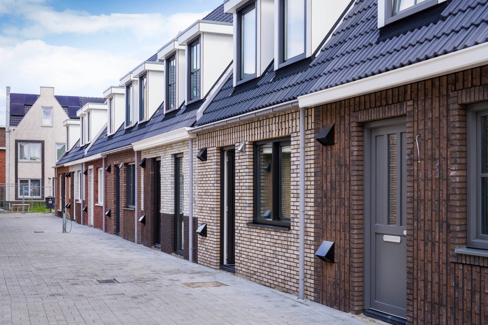 Foto van een straat met eenlaags met kap woningen in Parkwijk Lelystad. De gevels hebben allemaal verschillende kleuren gevelstenen. De woningen hebben twee dakkapellen op de eerste verdieping.
