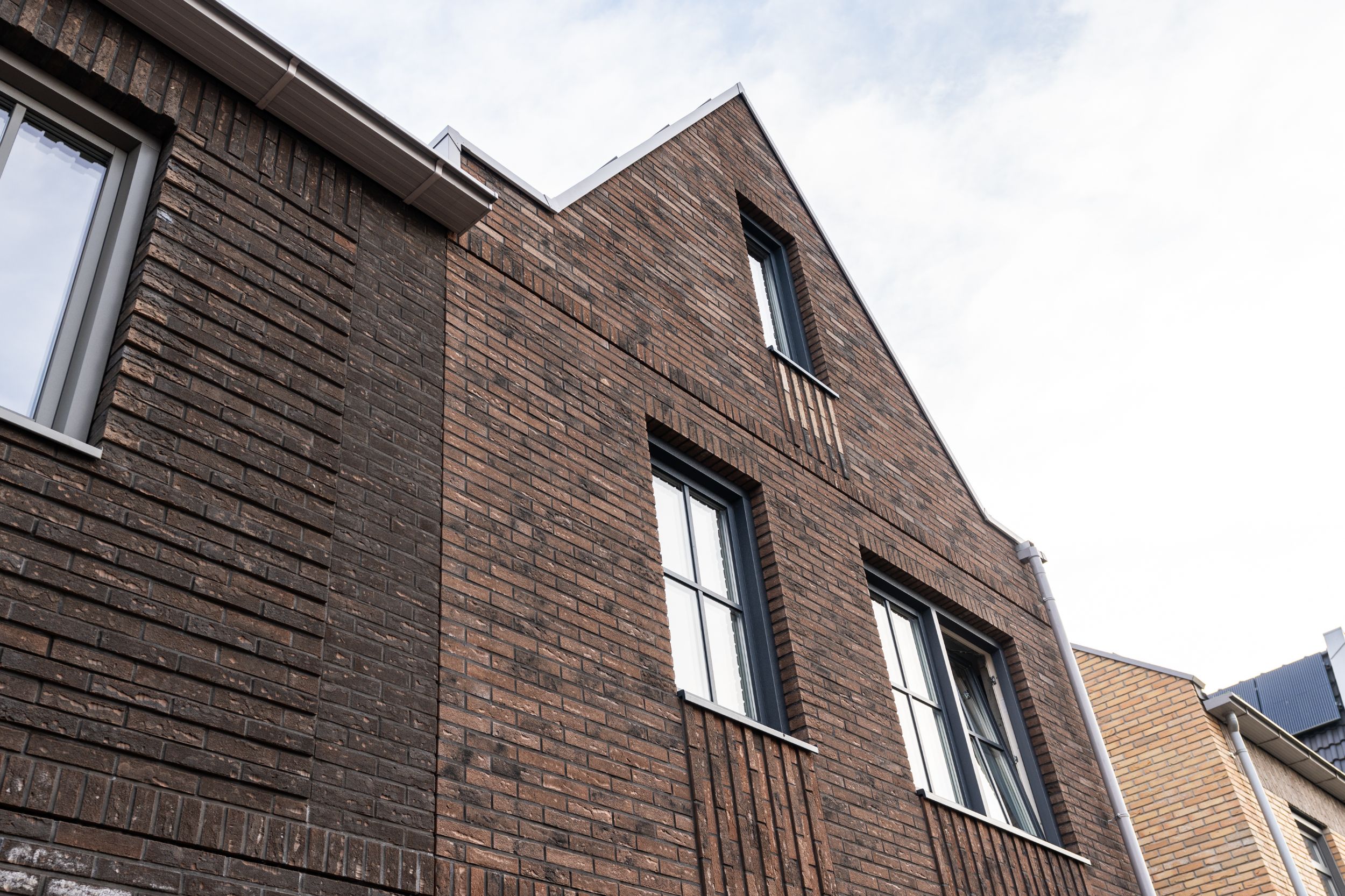 Foto van een tuitgevel van een van de tweelaags met kap woningen in Parkwijk Lelystad. Aan weerszijden zie je huizen met een ander gevelontwerp.