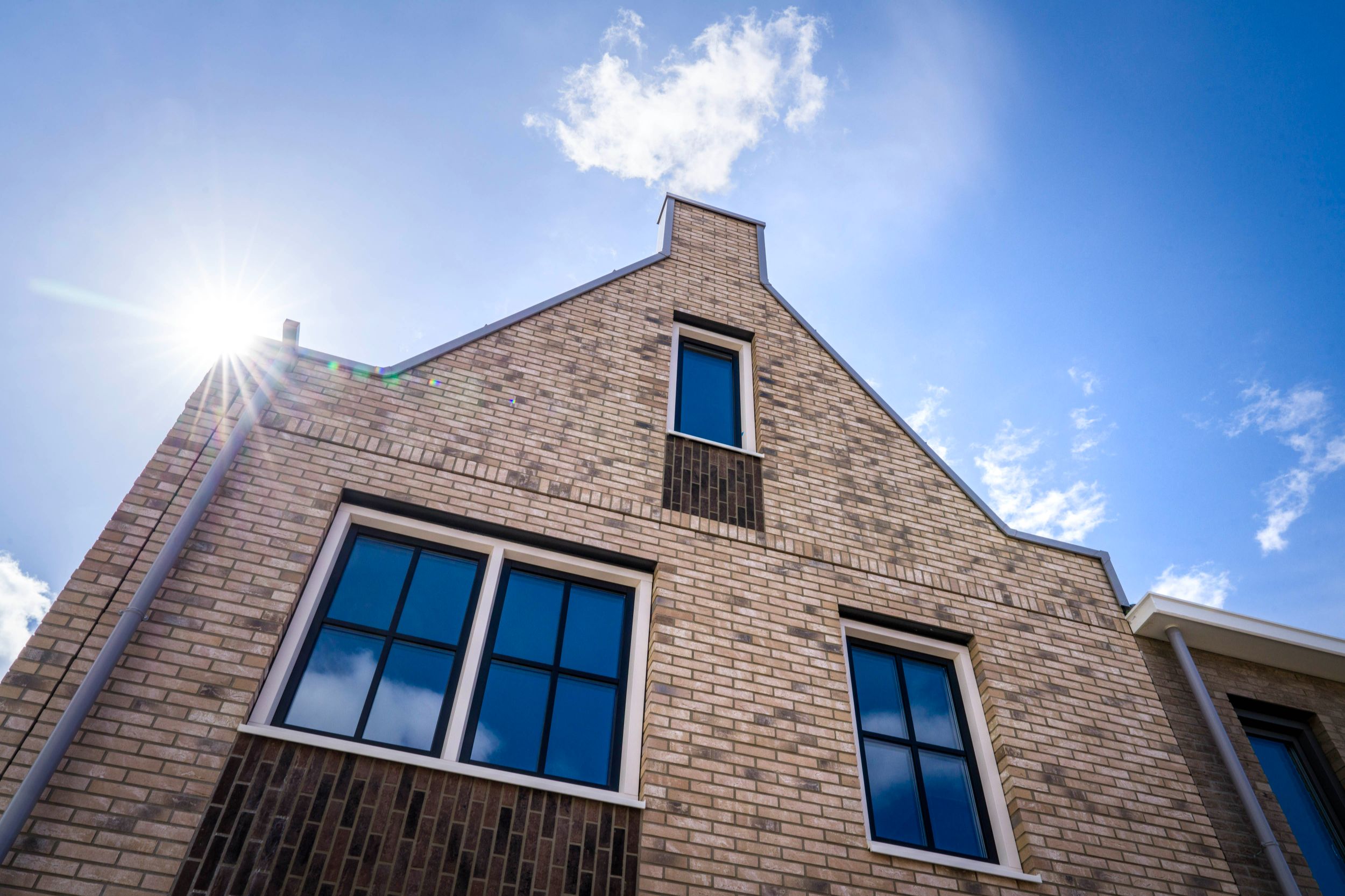 Een gevel van een tweelaags met kap woning met tuitgevel. De zon komt net boven de dakrand uit.