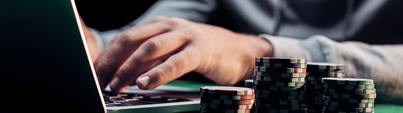 Person using a laptop for online gambling with stacks of poker chips beside them