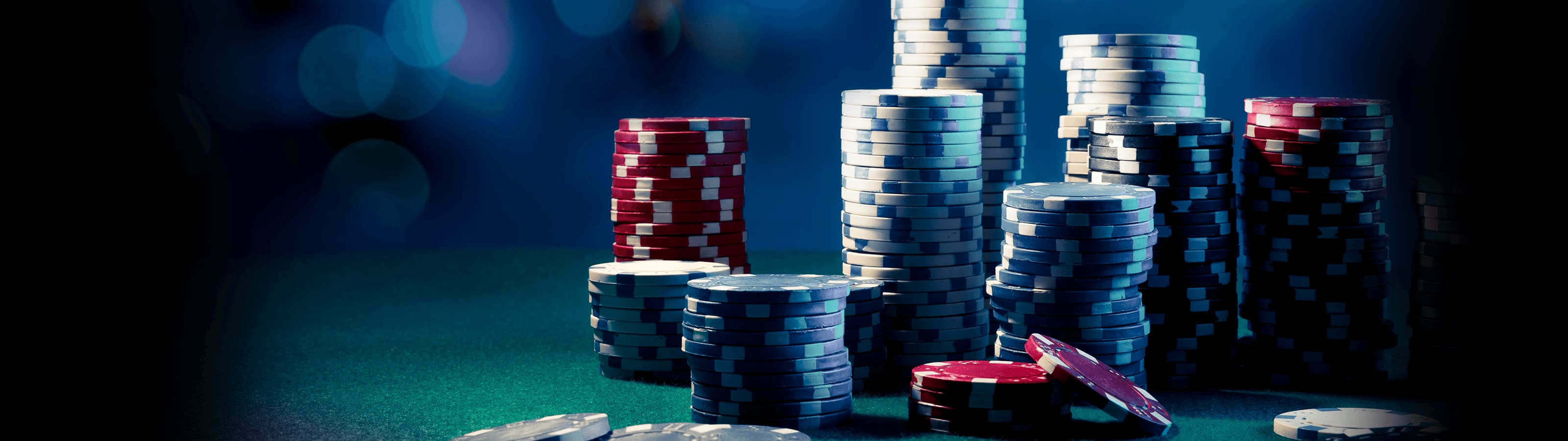 A close-up view of stacked poker chips in various colors on a green felt table, illuminated by dramatic lighting with a bokeh effect in the background