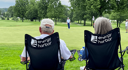 Man and woman watching golf players on putting green 