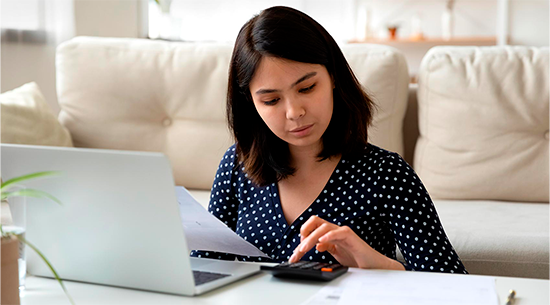 Woman calculating how to save on her electric bill with calculator and computer in front of her