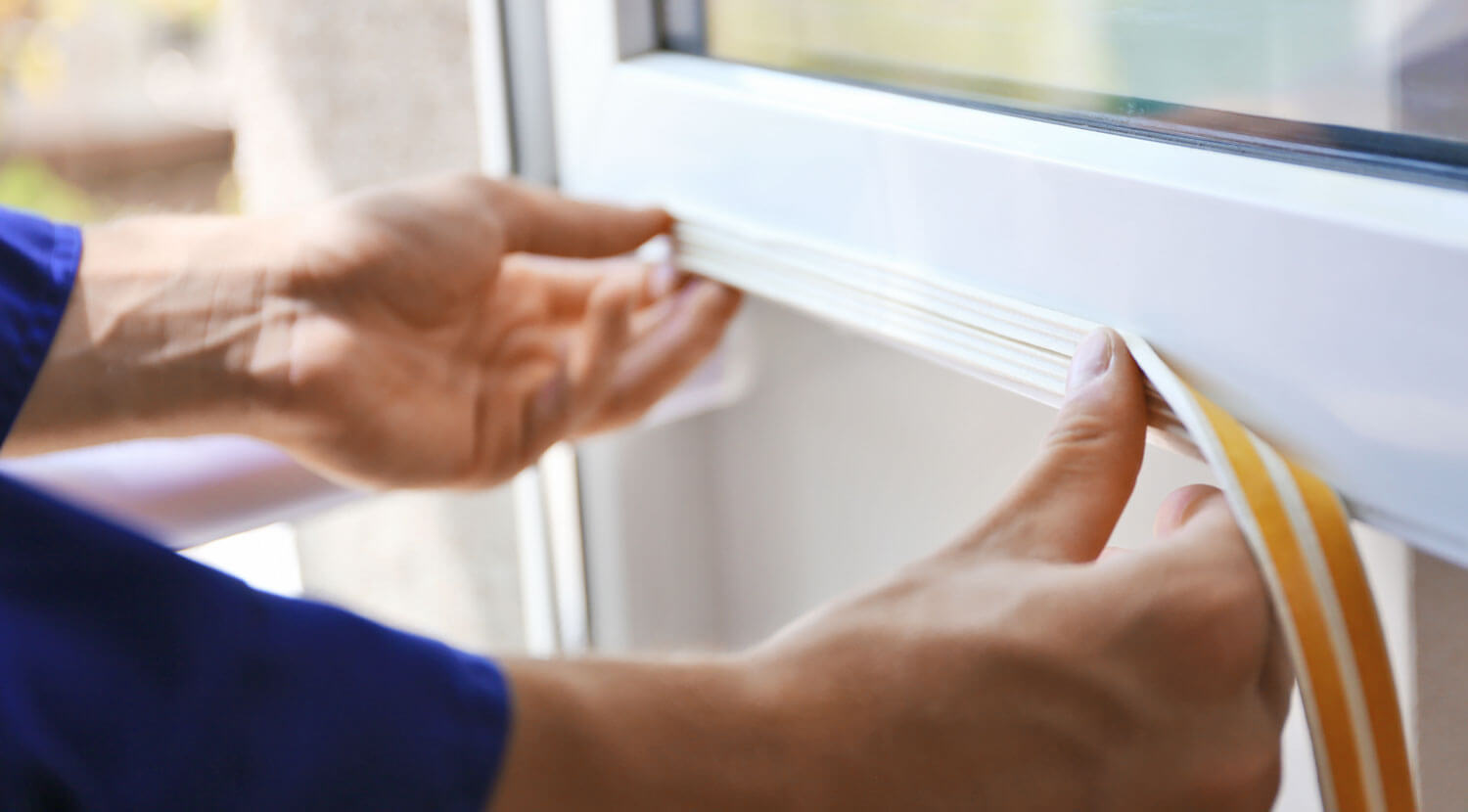A man’s hands installing weather stripping to a window.