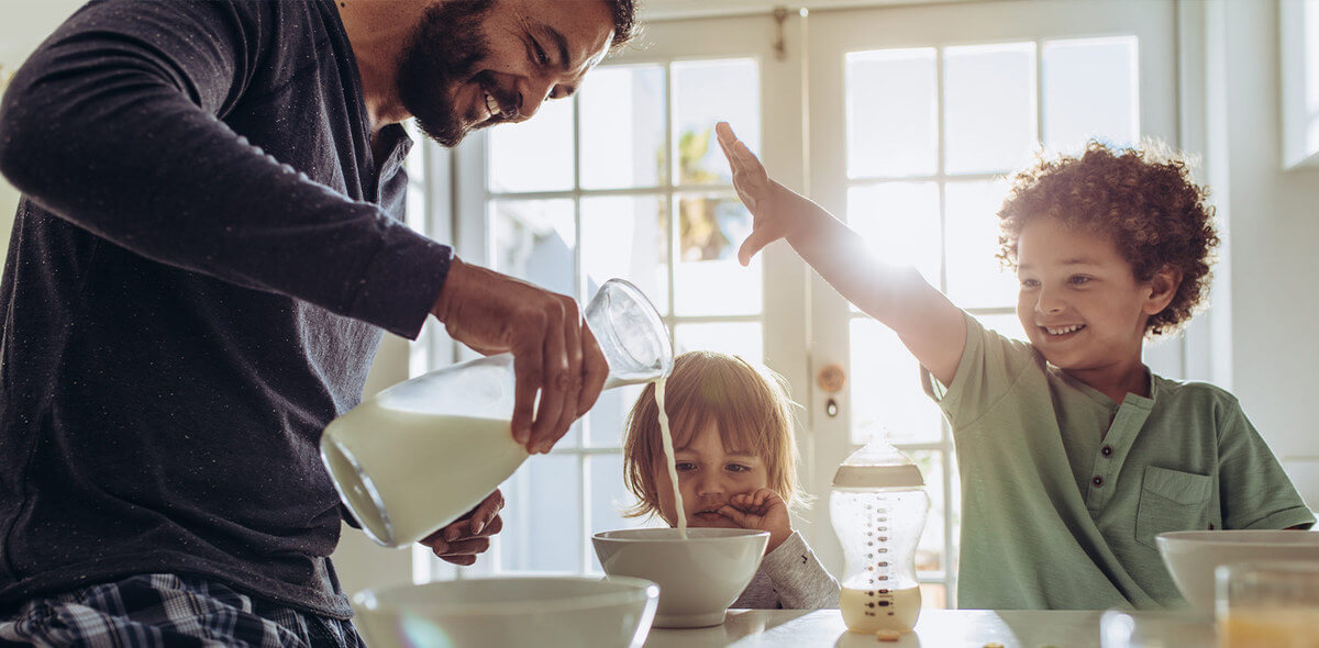 A father pours milk into a cereal bowl for his two children