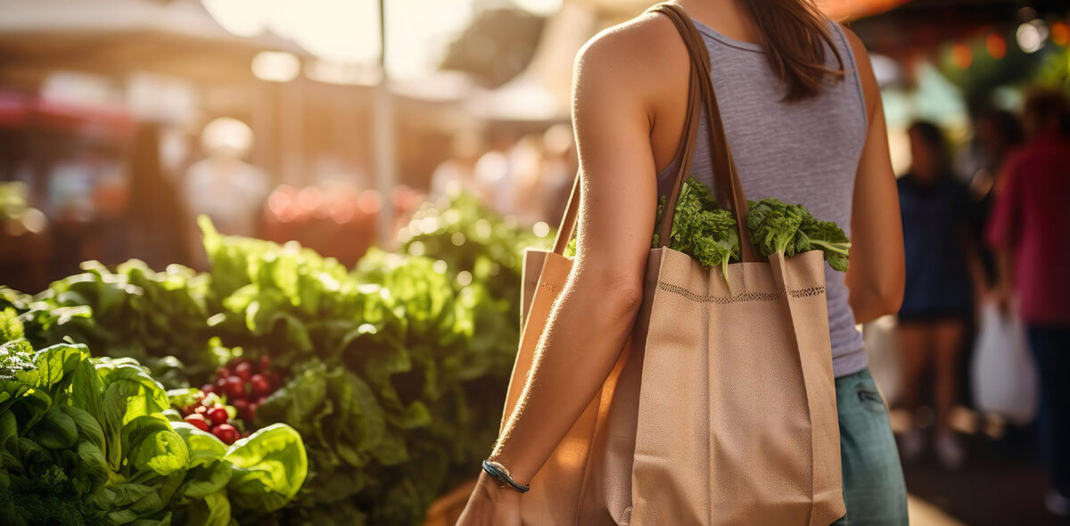 A woman with a shoulder bag shops in an outdoor produce market