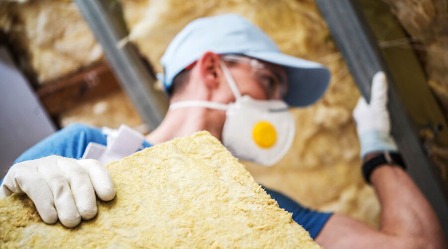 A man in a face mask installs attic insulation