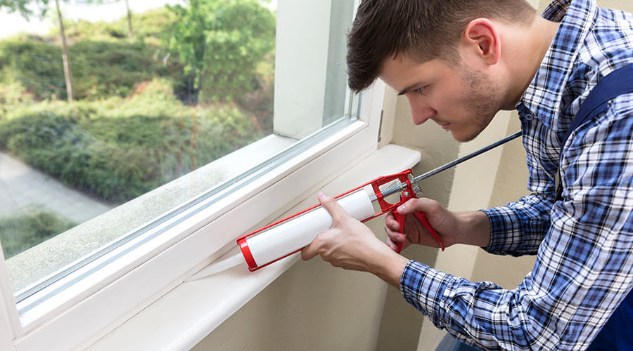 Man caulking to eliminate drafts around windows