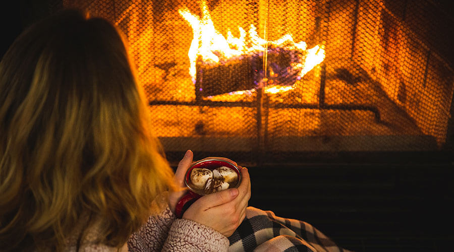 A woman enjoying cocoa in front of a fireplace