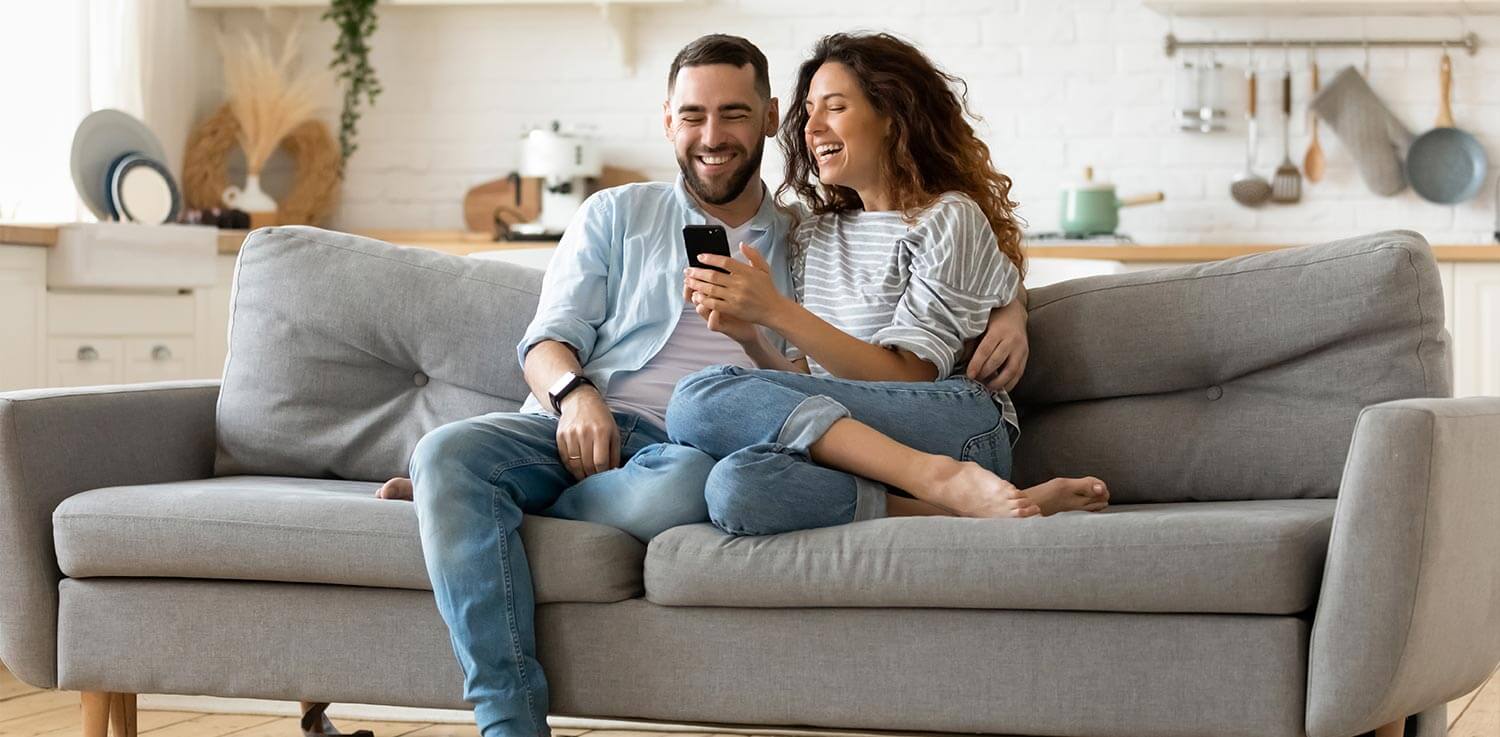 A couple relaxing on a couch compare rates on a smartphone