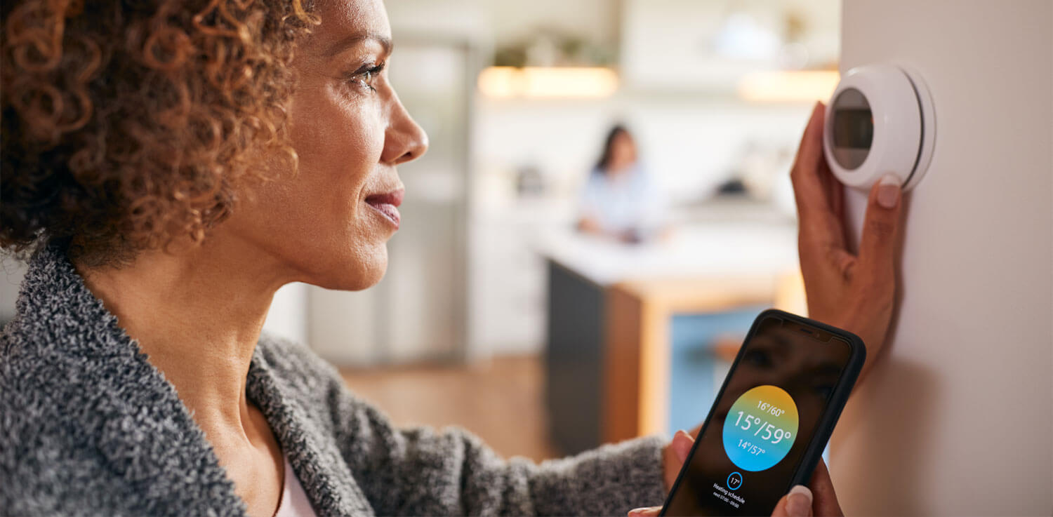 woman adjusting smart thermostat with phone 