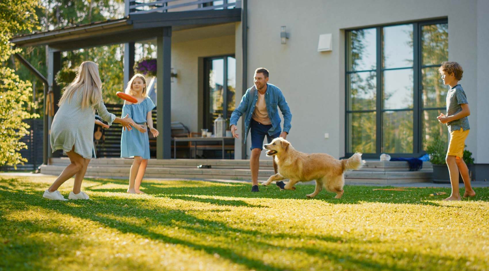 family throwing frisbee in yard with dog
