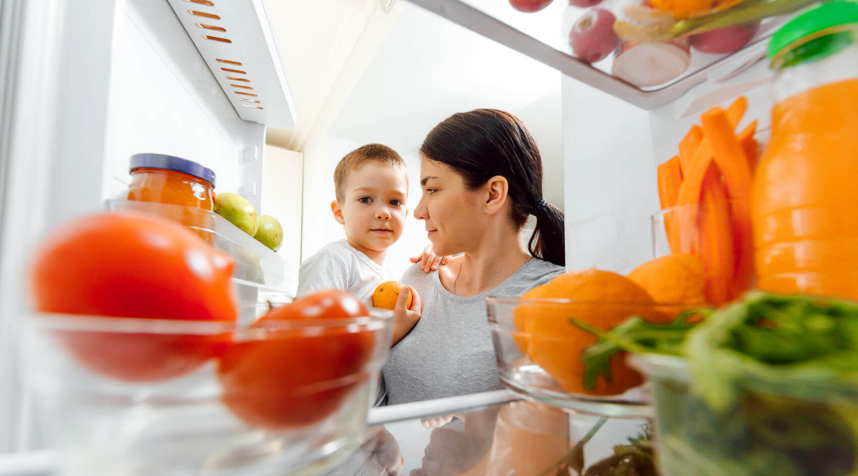 Mother holding child searches through refrigerator