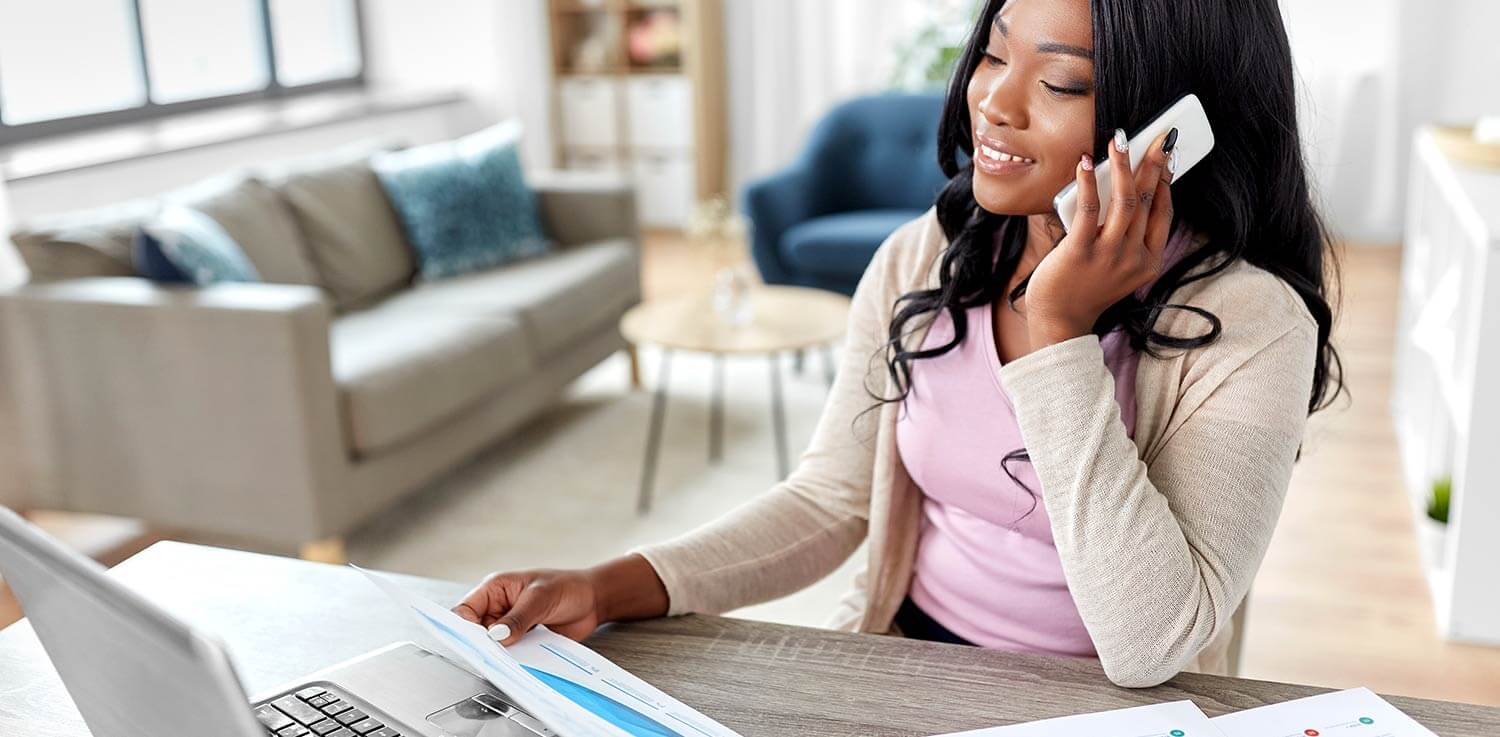 A young woman reviews her energy bill on her laptop while on the phone.