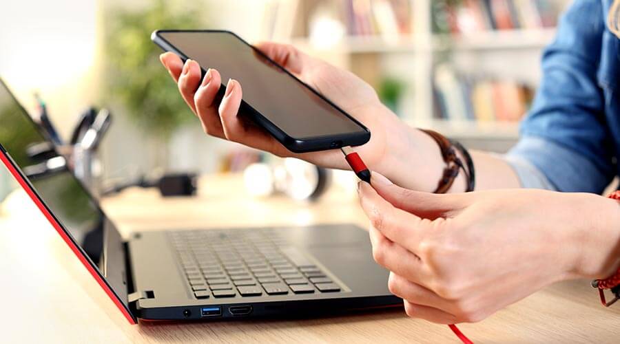woman plugging in cellphone to her laptop