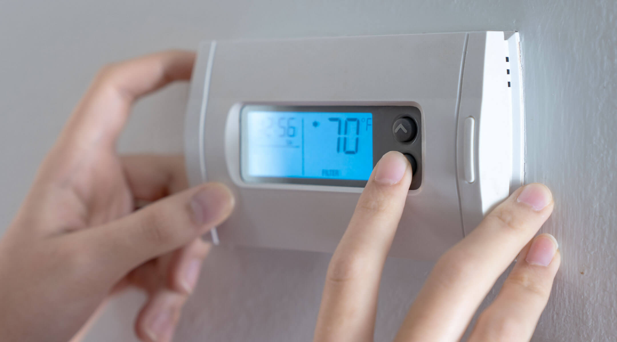 The hands of someone adjusting their home thermostat.