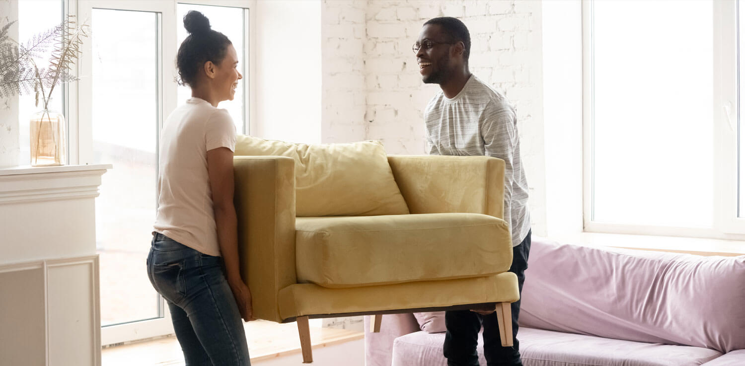 Couple rearranging furniture in living room carries big chair