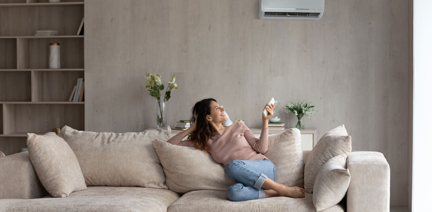 Woman sitting on couch uses remote to adjust air conditioner