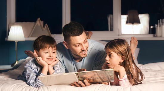 Dad reading to boy and girl on bed.