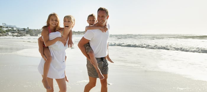 Mom and dad giving kids piggyback rides on the beach