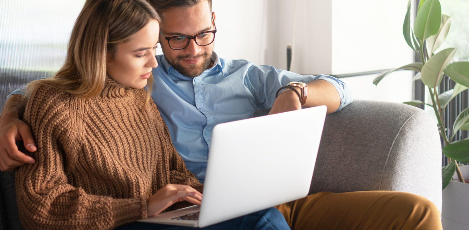 A woman and man sit on a couch and compare electric rates on a laptop.