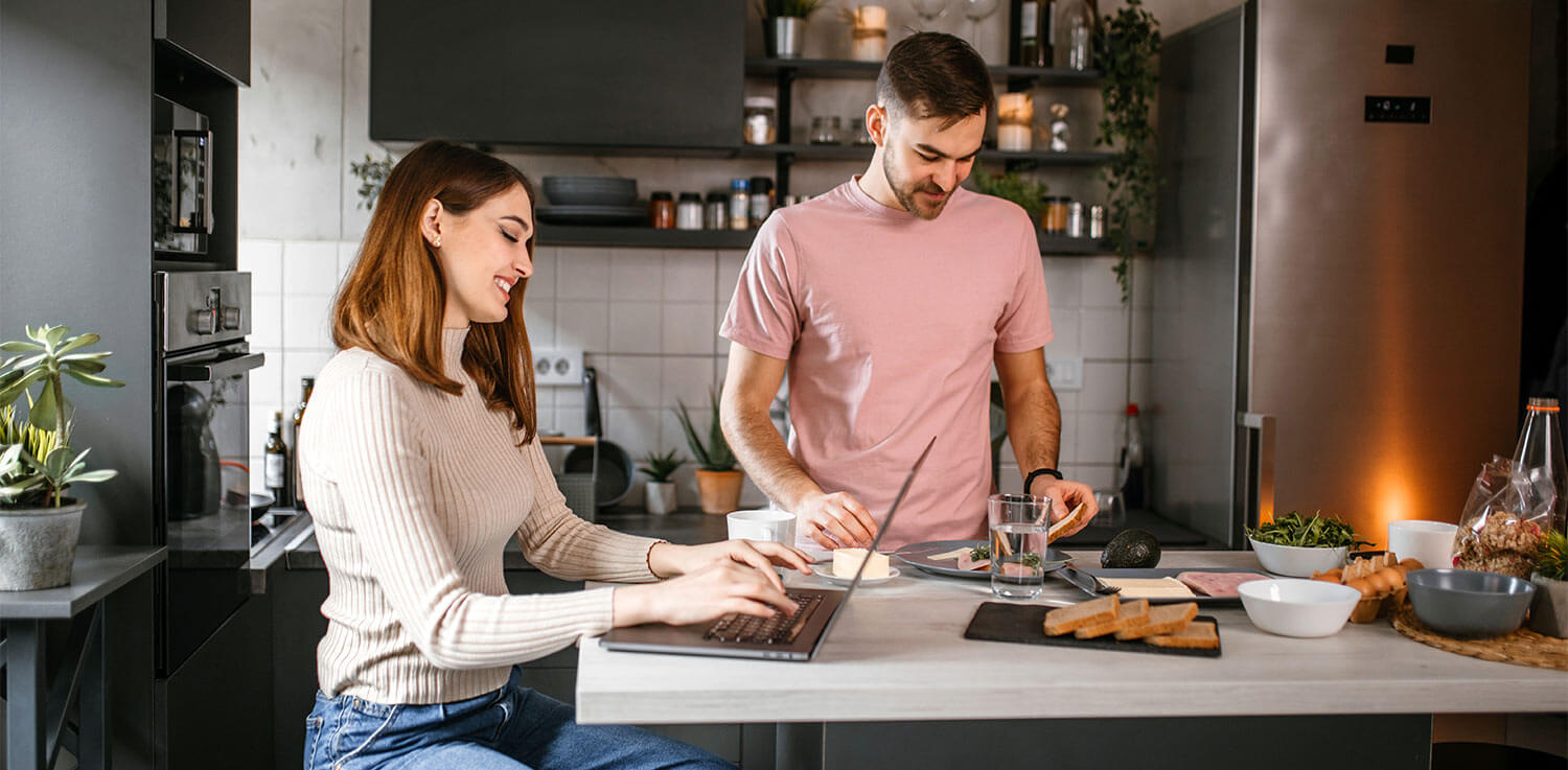 woman using computer at kitchen island with man making sandwitch 