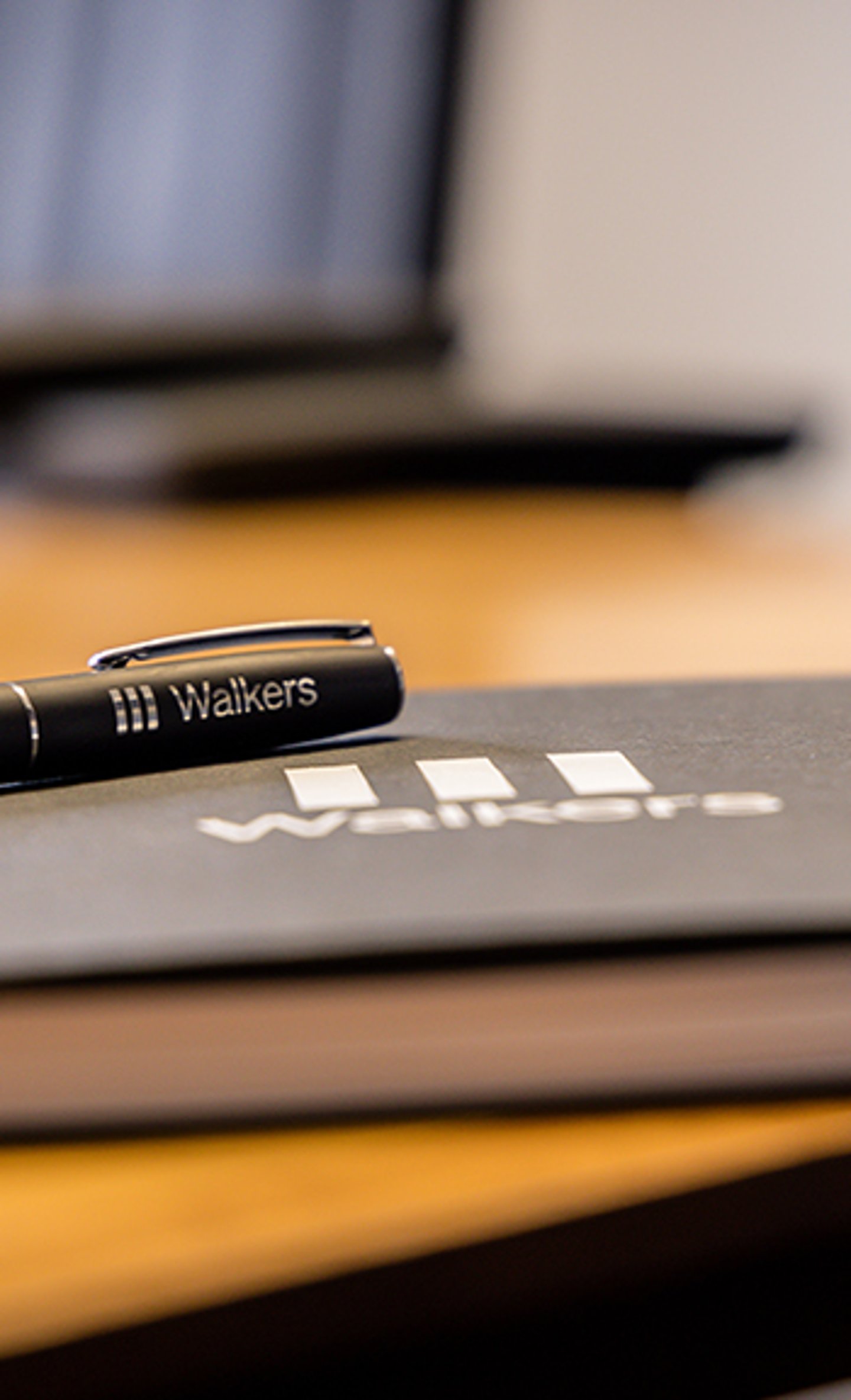 A sleek black pen with 'Walkers' branding lies atop a closed notebook, both featuring raised 'Walkers' logos.