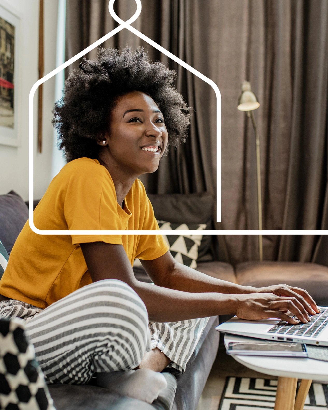 Young girl sitting on the couch, smiling as she works on a laptop.