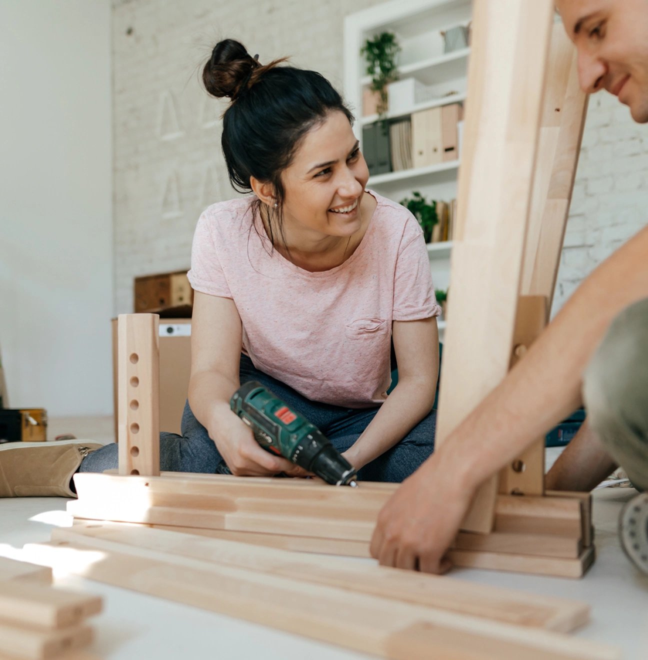 A young woman uses a power tool as she helps her partner with a home DIY project.