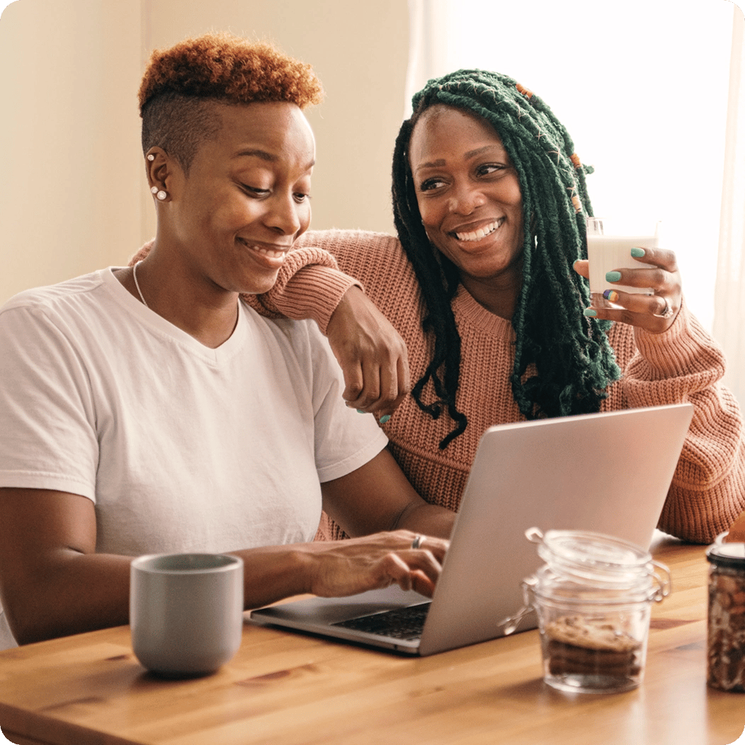 Two young women sit together at a table as they happily research accident insurance options.