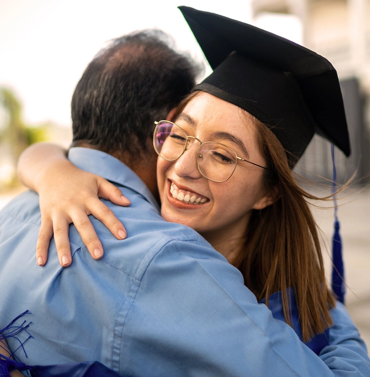 A smiling girl in a graduation cap hugs her father at a graduation ceremony.