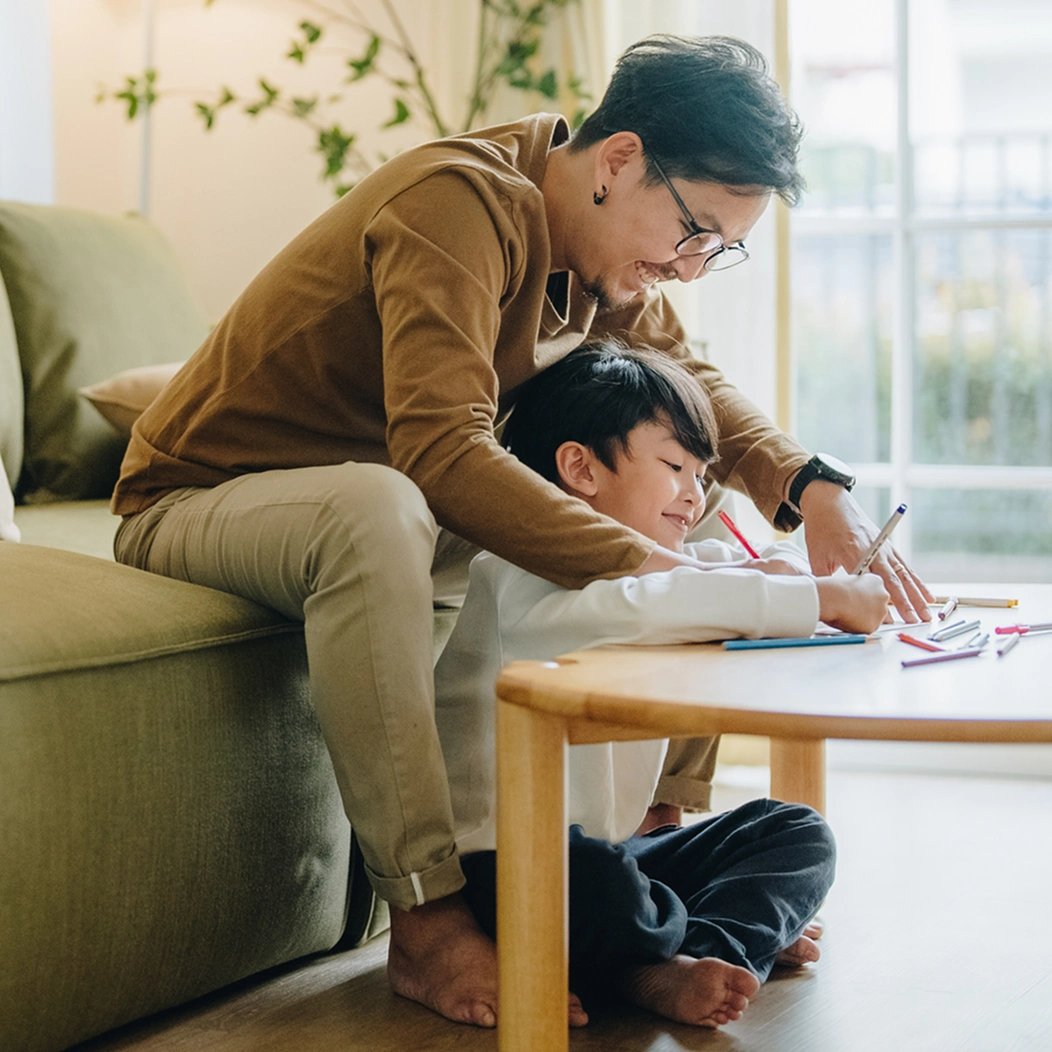 A young father sits with his son as they use markers to color activity sheets.