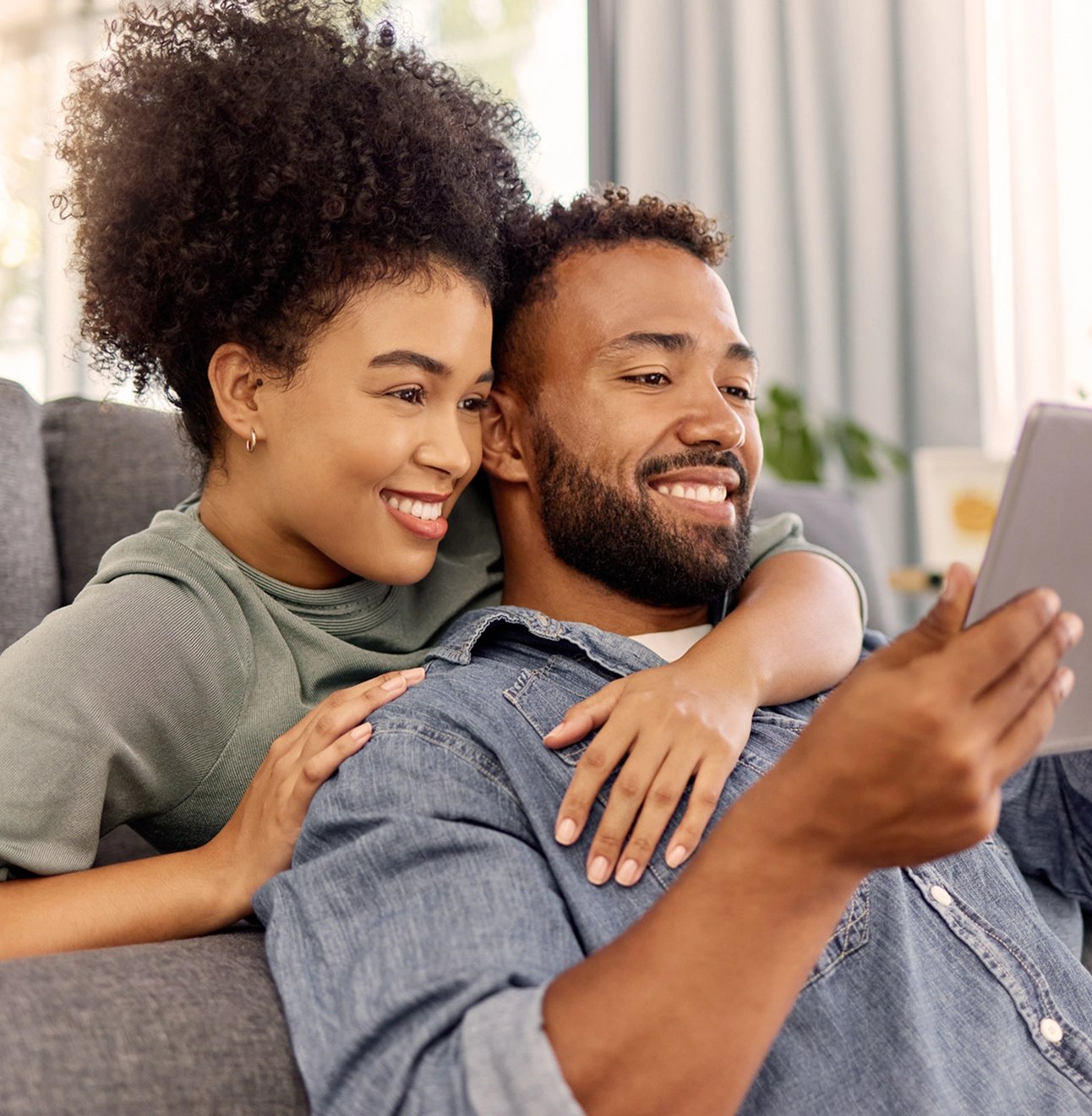A trendy young couple sits on a couch and researches digital wills and other estate planning options on a smartphone.