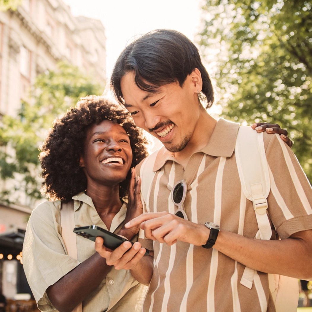 A young couple walks outdoors and uses a smartphone to look up information about digital wills.