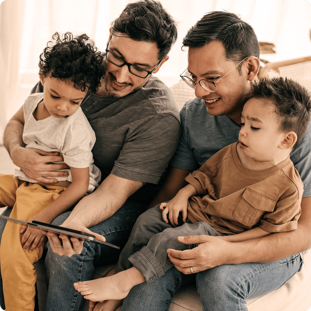 Young parents hold their kids on their laps, reviewing the details of their family term life insurance on a tablet.