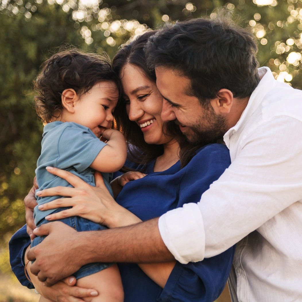 A mom and dad share a group hug with their young toddler, happy because they selected the best whole life insurance for kids.