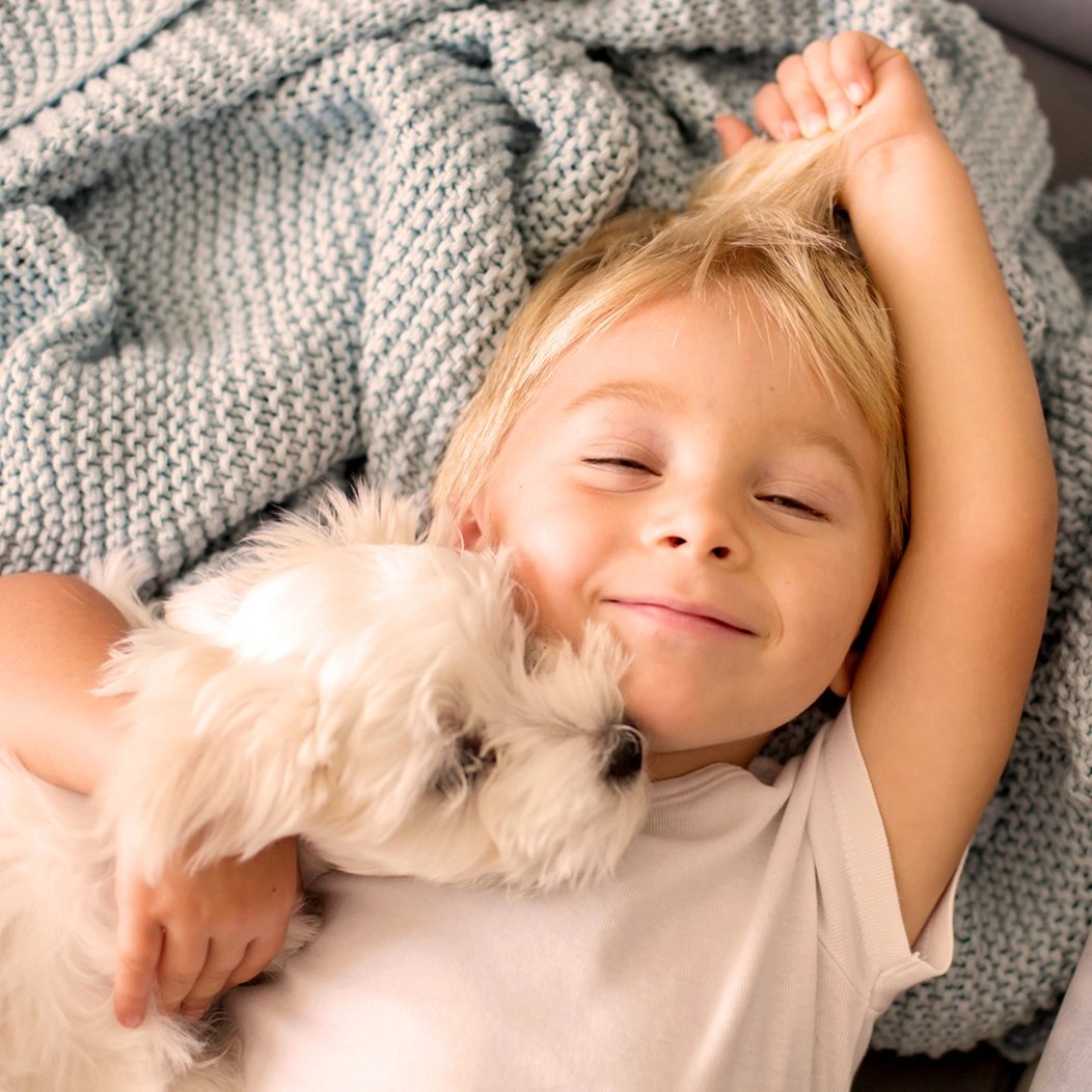 Smiling toddler, who has a whole life insurance policy for children that builds cash value over time, cradles a small, white puppy.