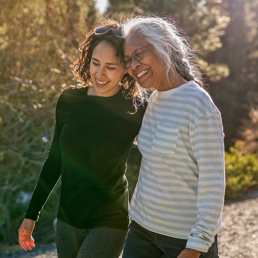Adult daughter walks with her mother outdoors as they discuss guaranteed life insurance options.