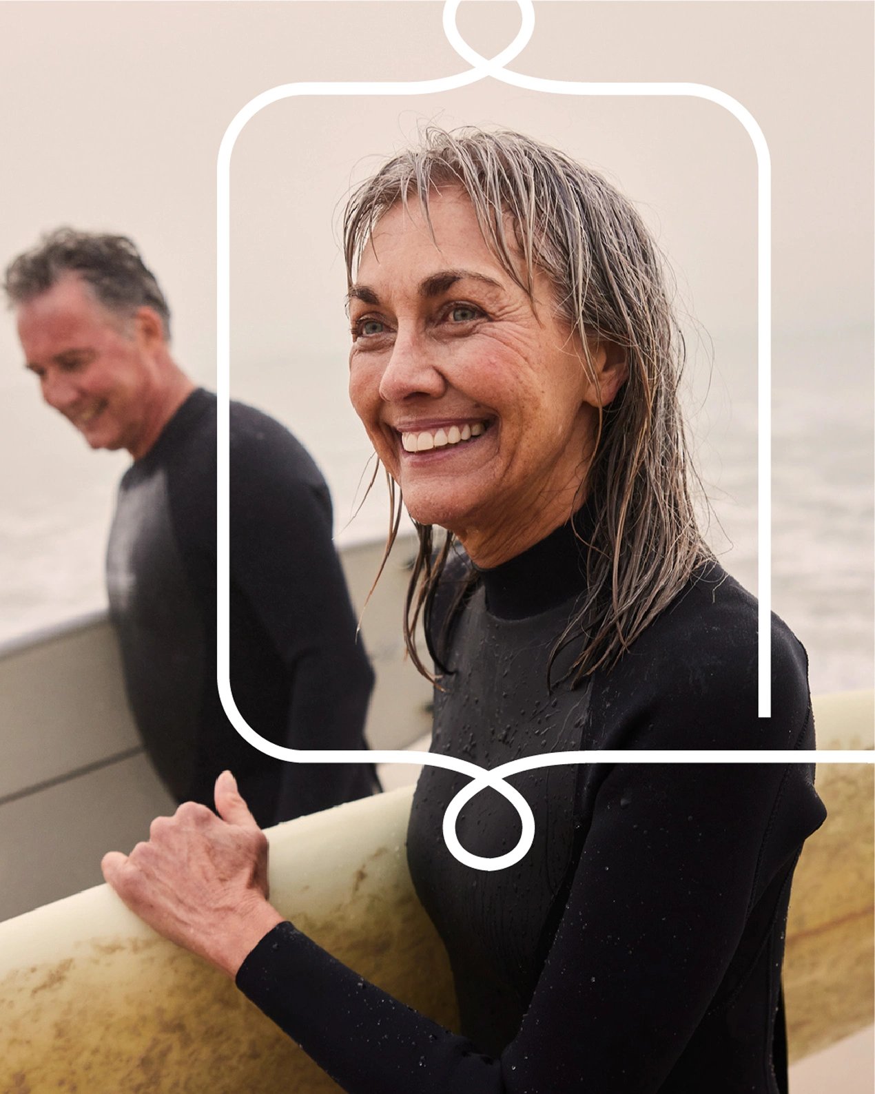 Older woman with a guaranteed life insurance policy smiles as she walks with her surfboard from the ocean.