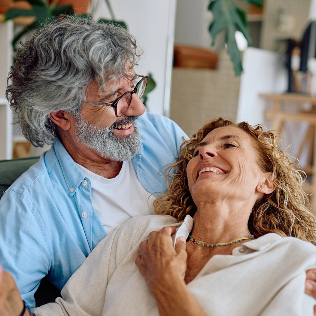 Happy couple share a laugh on their couch, thankful for their guaranteed acceptance life insurance coverage.