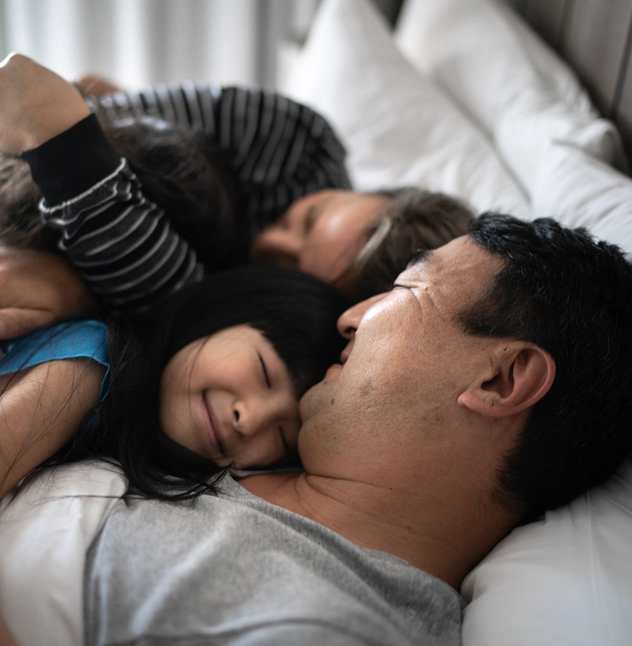 A mom and dad nuzzle their young toddler, who's smiling.