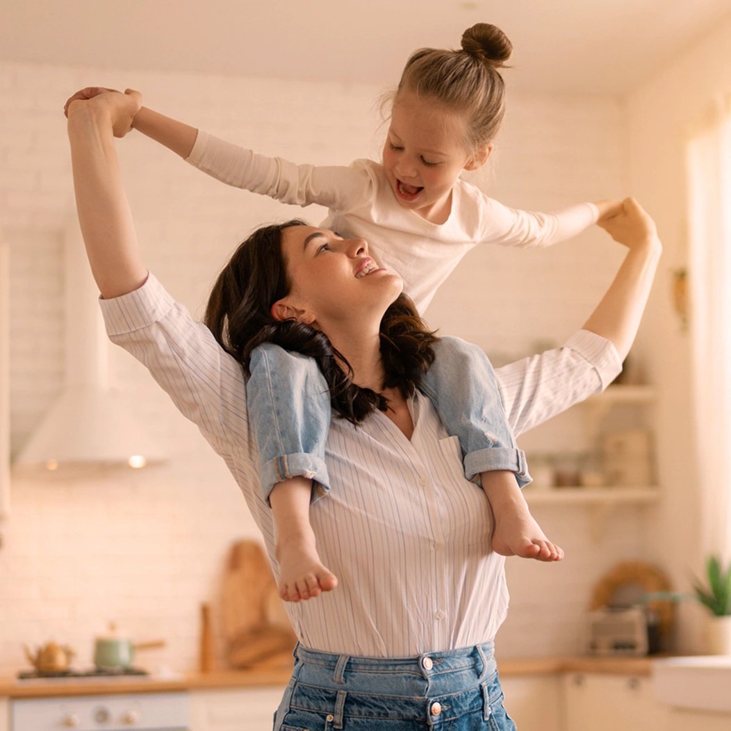A young mother carries her small daughter on her shoulders as they smile and laugh, secure in the protection of their term life insurance coverage.