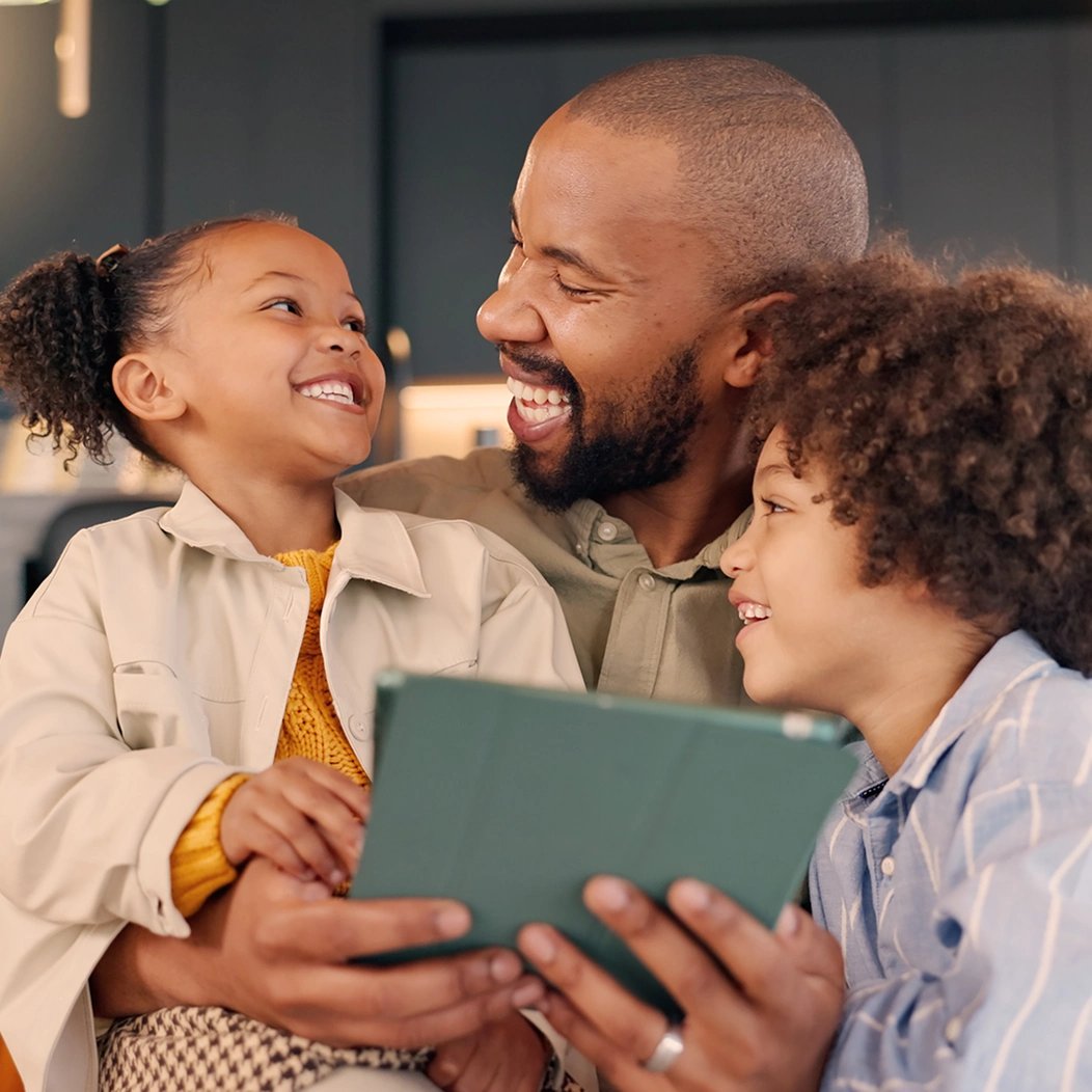 A father spends time outdoors with his two young children, smiling and laughing.
