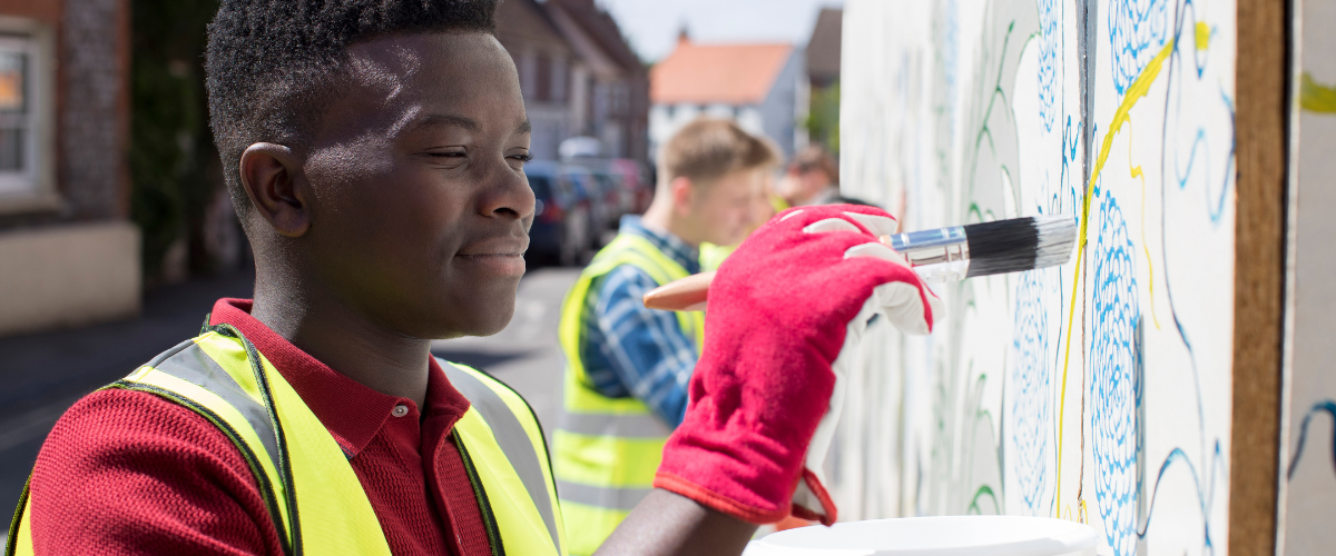 Student volunteering and painting a mural on a fence