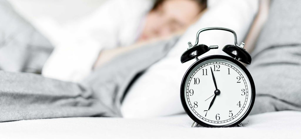 A person sleeping in bed next to an alarm clock showing the time