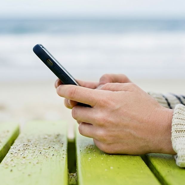 Person nutzt ein Smartphone an einem Tisch im Freien