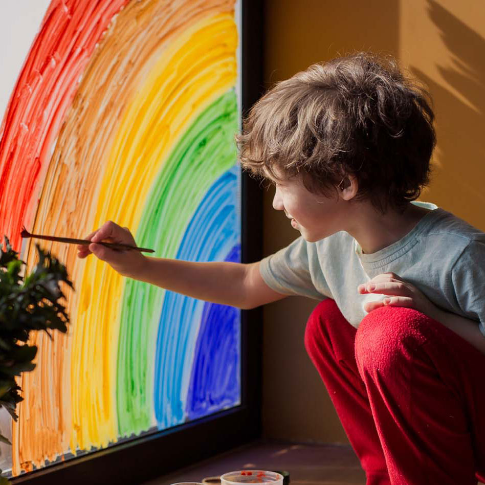 boy painting rainbow on glass window