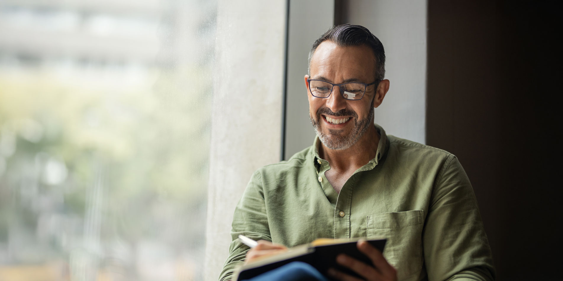 smiling man with glasses writing in notebook
