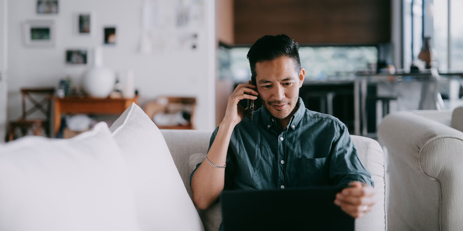 man talking on the phone and sitting on a couch with laptop 